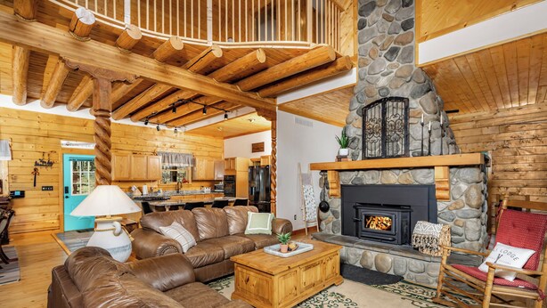 Un intérieur chaleureux de chalet avec une cheminée en pierre, des poutres en bois au plafond, un canapé en cuir et un coin repas.
