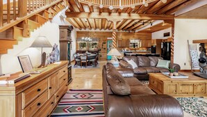 Un vaste espace de vie agrémenté d’un escalier en bois, d’un canapé en cuir et d’un coin repas illuminé par un lustre.