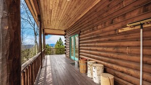 Une cabane en bois dotée d’une terrasse en bois, d’une porte avec des panneaux de verre et offrant une vue sur les arbres et les montagnes.