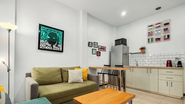 A modern kitchen with a dining area, a sofa, and a small table. - One Apartments TLV (Tel Aviv)