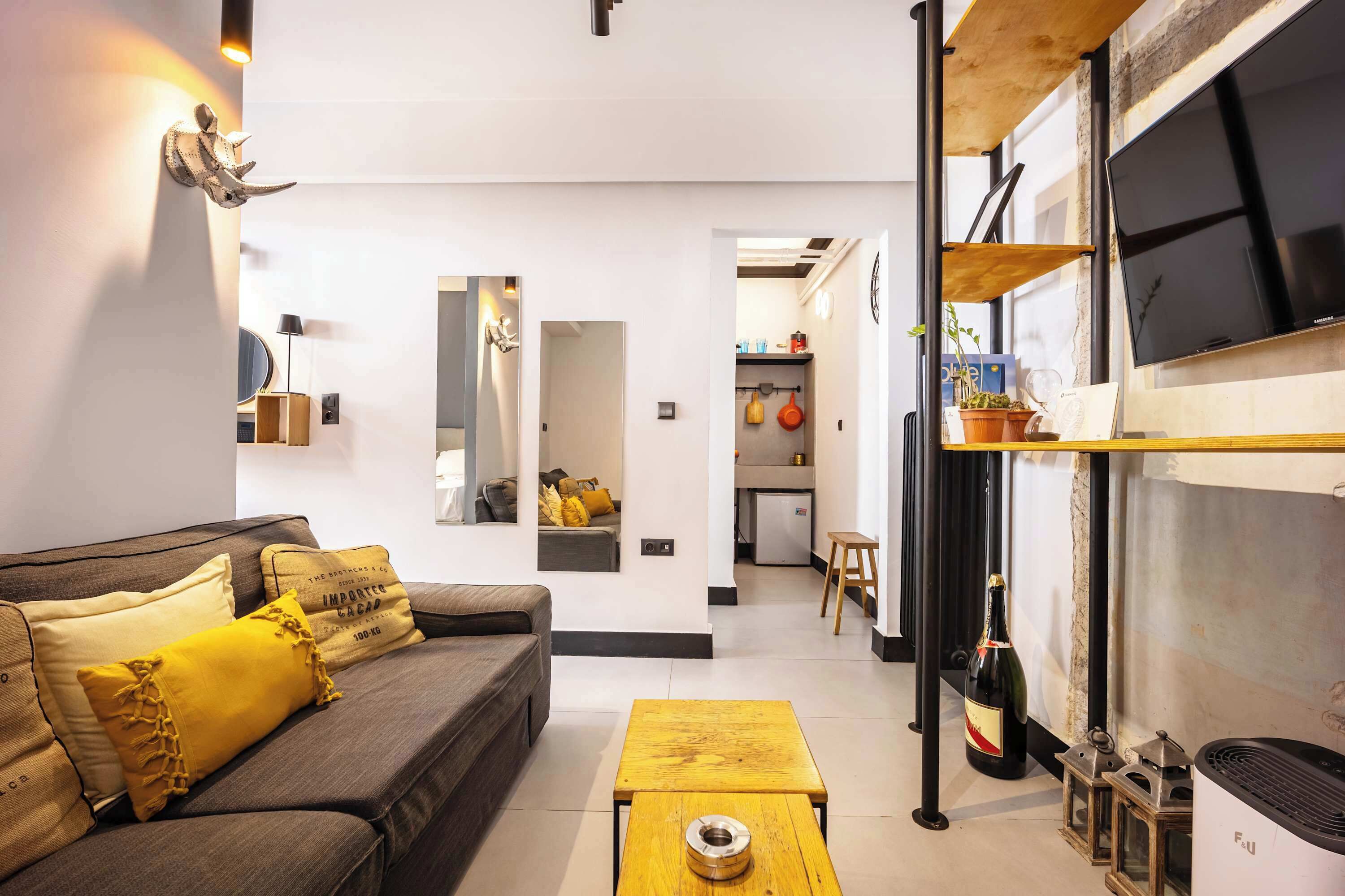 A modern living room with a sofa, a coffee table, and a kitchen area visible through an open doorway.