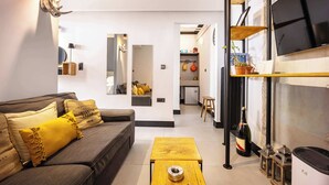 A modern living room with a sofa, a coffee table, and a kitchen area visible through an open doorway. - Well Designed 1BR in Prime Kolonaki (Athina)