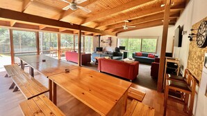A spacious living area with wooden beams, large windows, and a dining table. - Albaski Lodge – Room 4 (Sawmill Settlement)