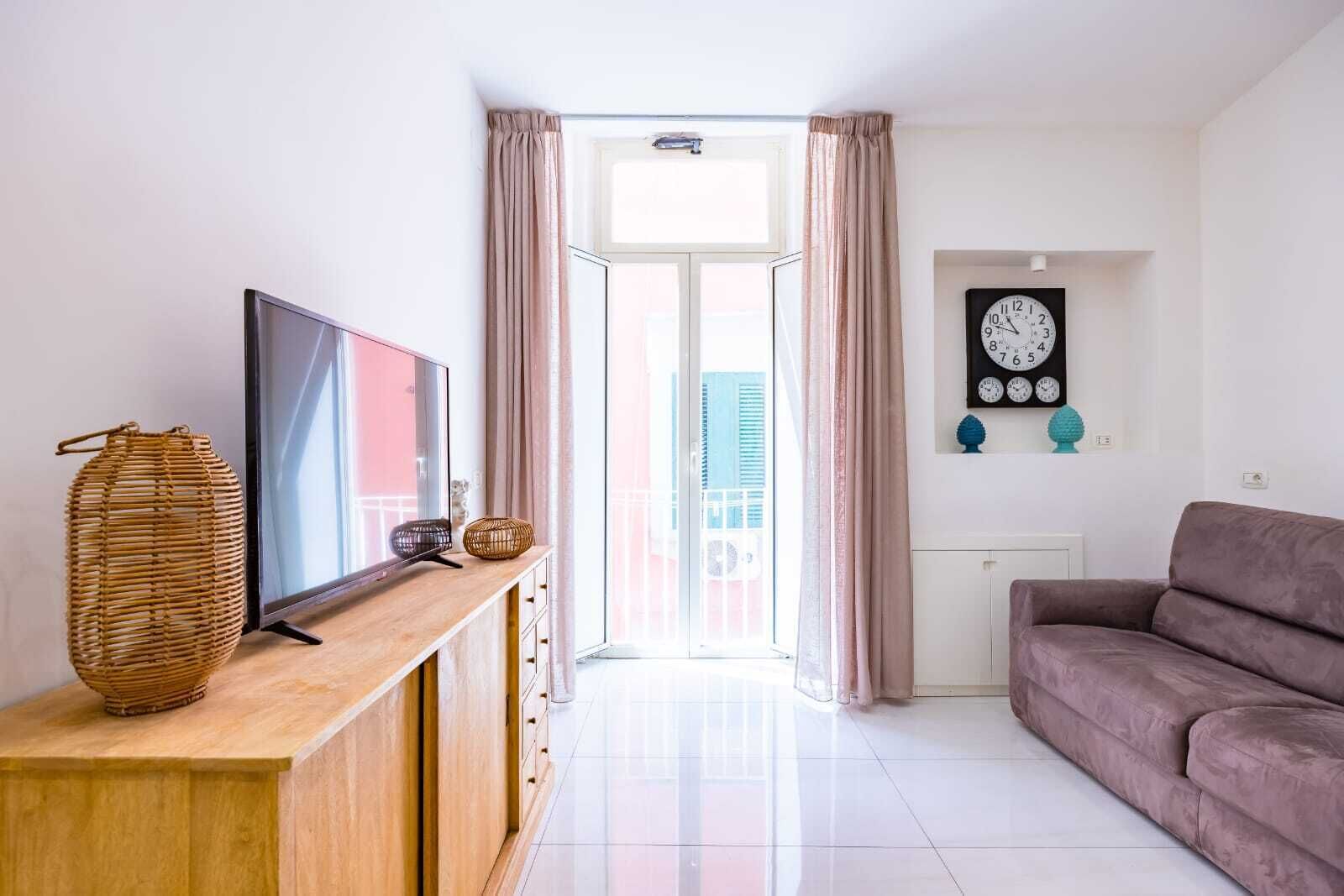 Ein modernes Wohnzimmer mit einem Flachbildfernseher auf einer Holzkonsole, einer Korbvase, einem Sofa und einer Wanduhr.