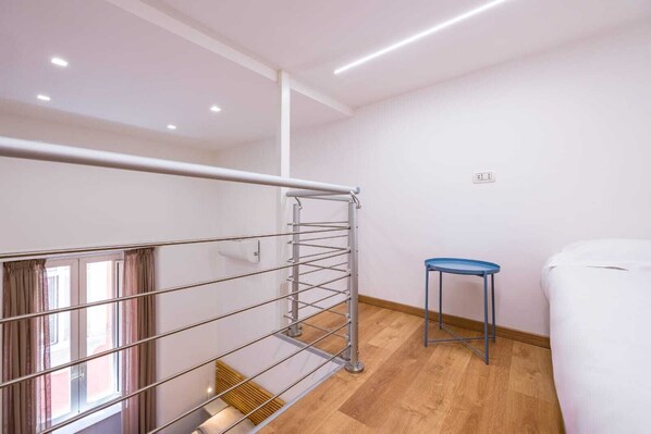 A modern room with a metal staircase, a small blue stool, and a white bed. - Appartamentino ai quartieri spagnoli (Naples)