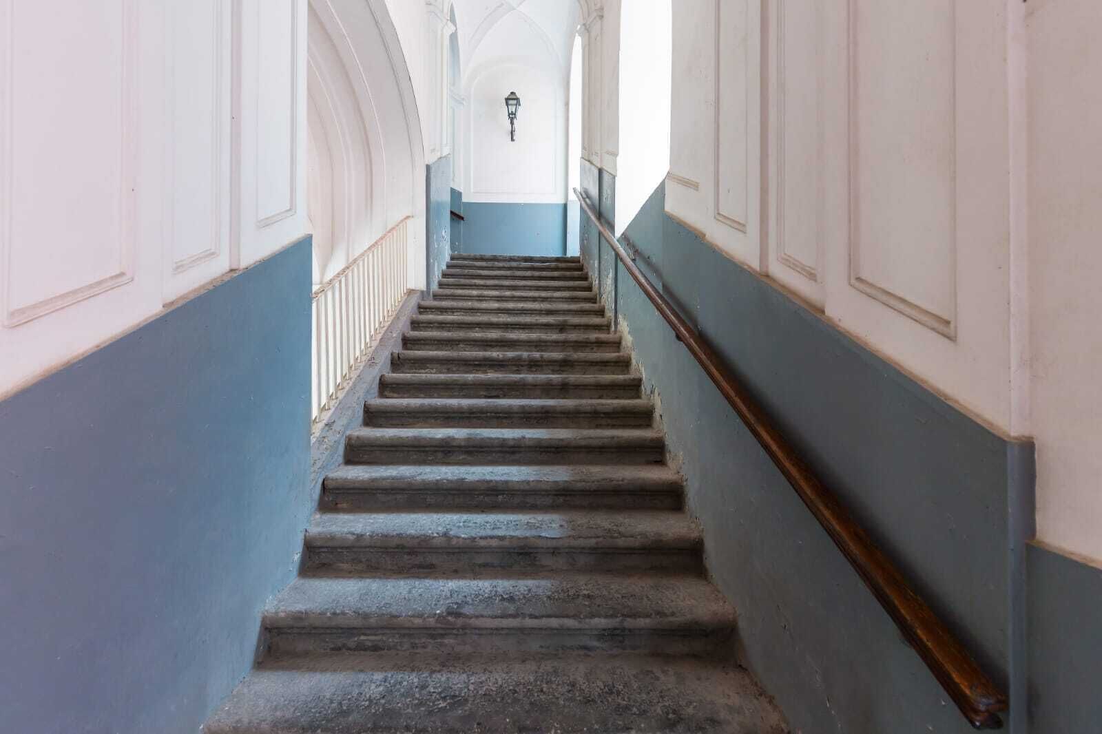 A long, narrow staircase with a wooden handrail and a light fixture at the top.