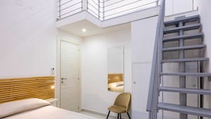 Ein Schlafzimmer mit Bett, Stuhl, Spiegel, Tür und Treppe.