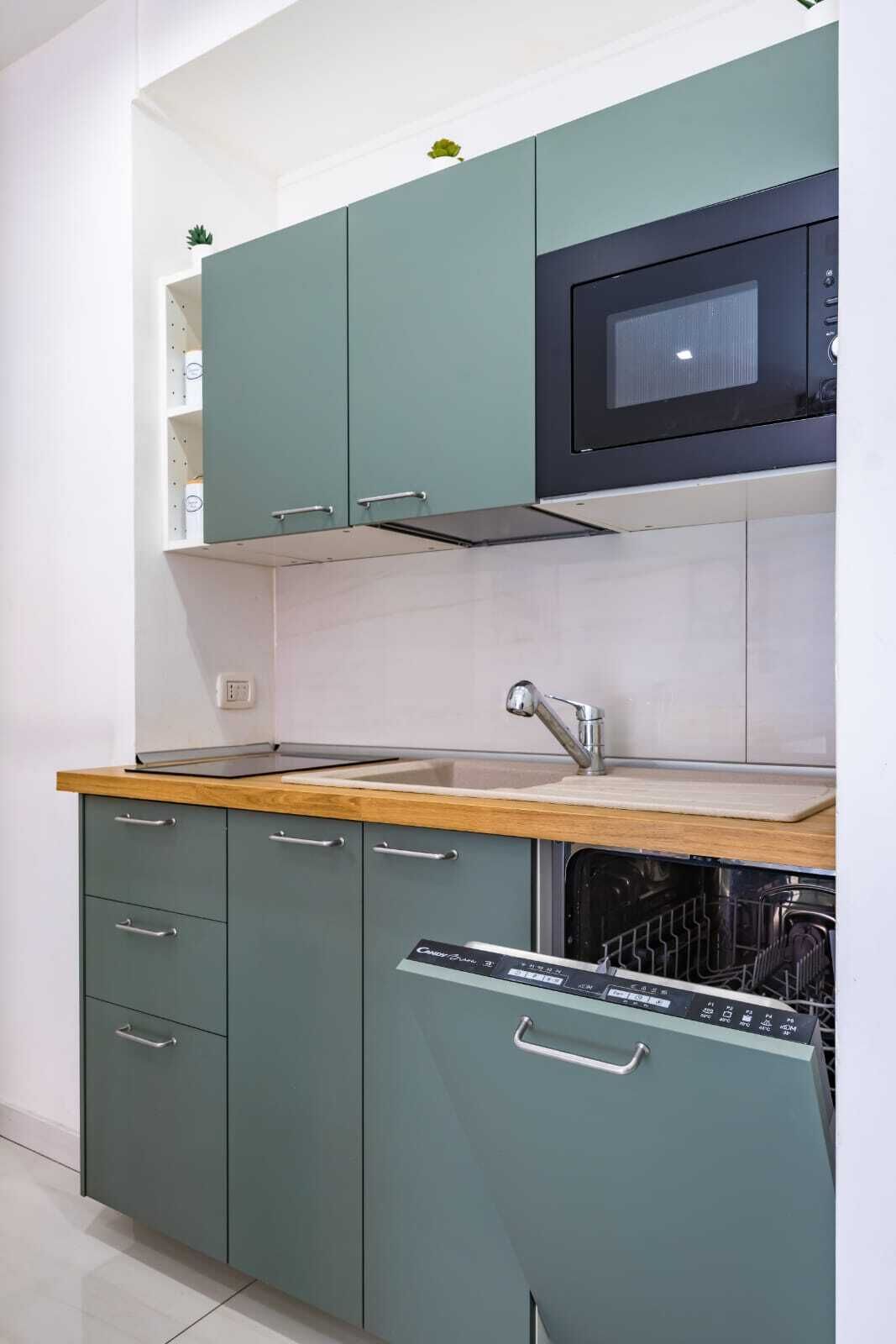 A kitchen with teal cabinets, a microwave, a sink, and a dishwasher.