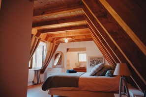 A bedroom with a sloped ceiling, a bed, a bedside table, a lamp, and a window.
