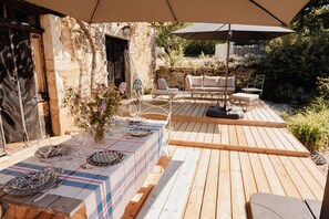 An outdoor wooden deck with a table set for dining, a wicker chair, and an umbrella.