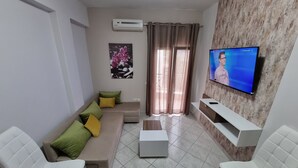 Un salon moderne avec un canapé d’angle beige, deux fauteuils blancs, une table basse et un téléviseur à écran plat fixé sur un mur à texture.