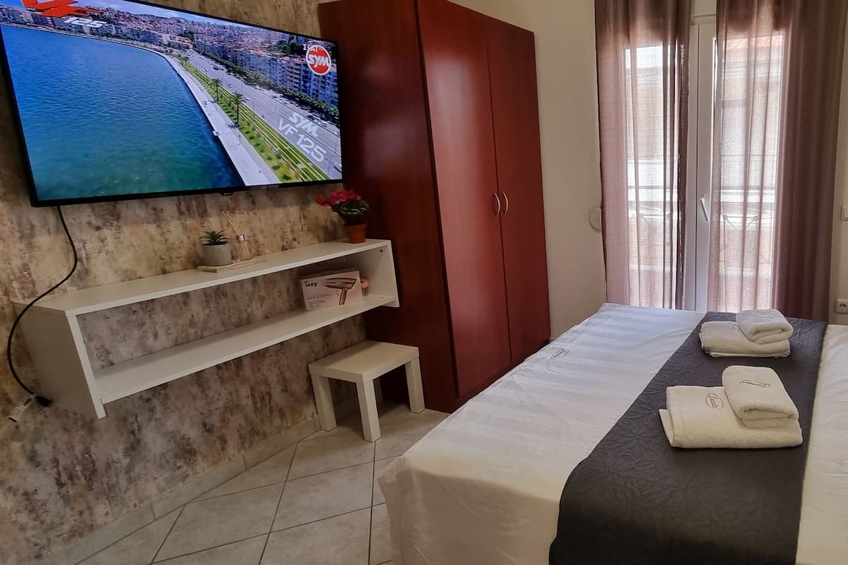 Een hotelkamer met een bed, een aan de muur bevestigde televisie, een garderobe en een raam met gordijnen.