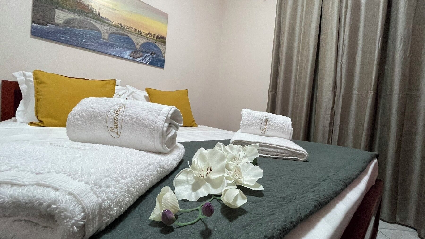 Habitación de hotel con dos camas, toallas blancas, colcha verde y una pintura de un puente sobre el agua.