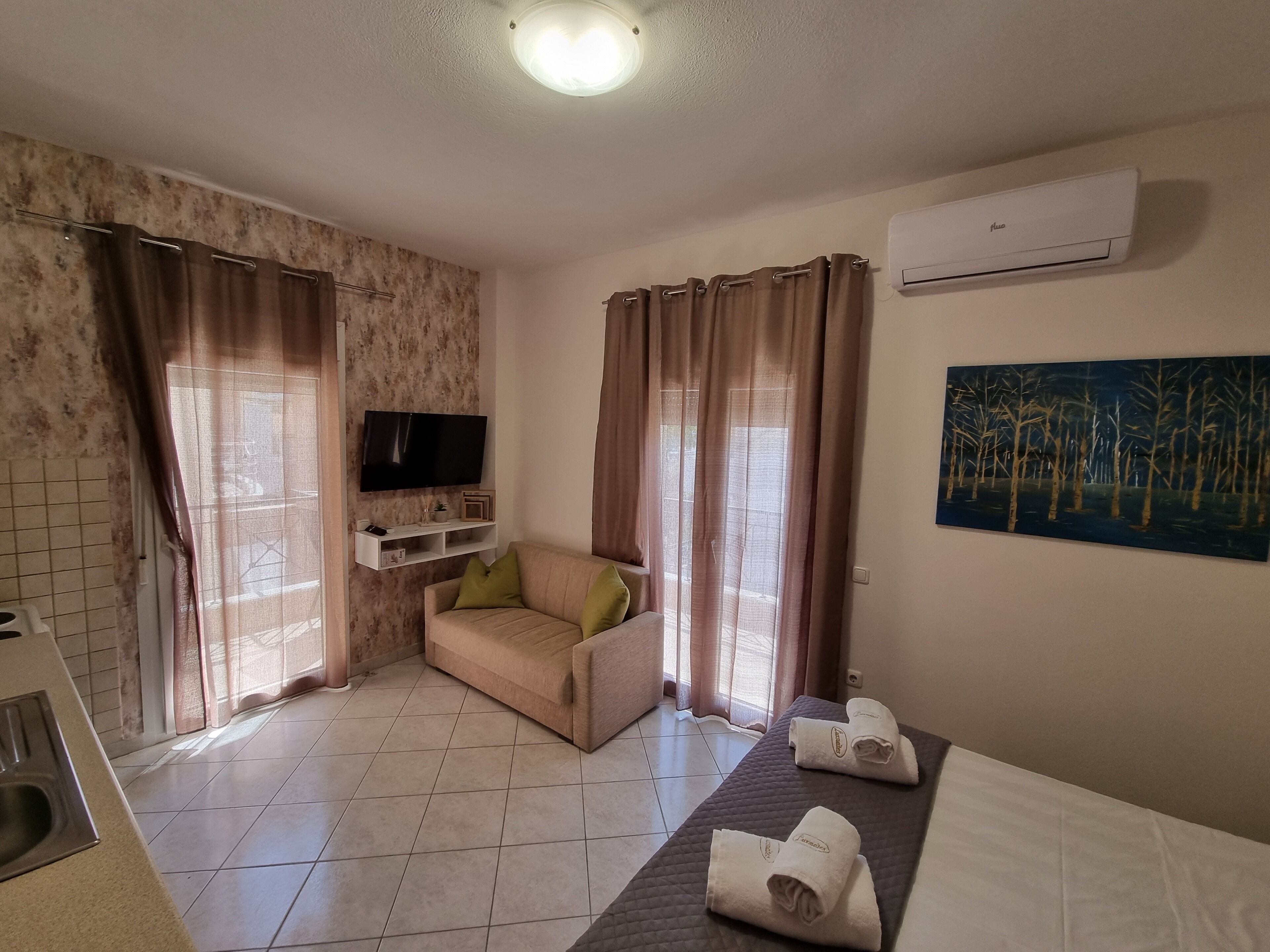 Habitación de hotel con sofá beis, un televisor de pantalla plana, un cuadro y una cama con toallas.