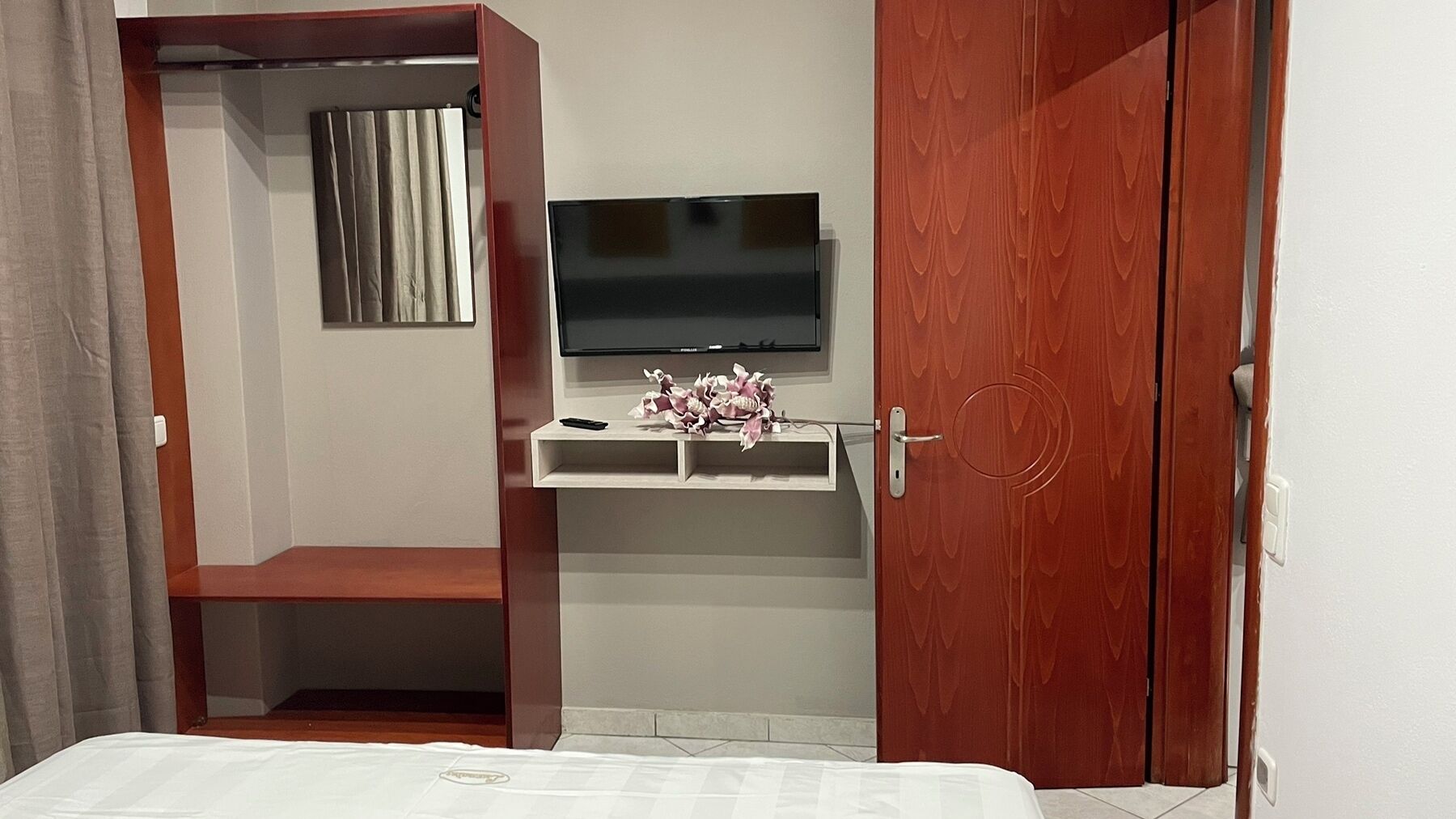 A bedroom with a bed, a TV on a shelf, a wardrobe, and a curtain.