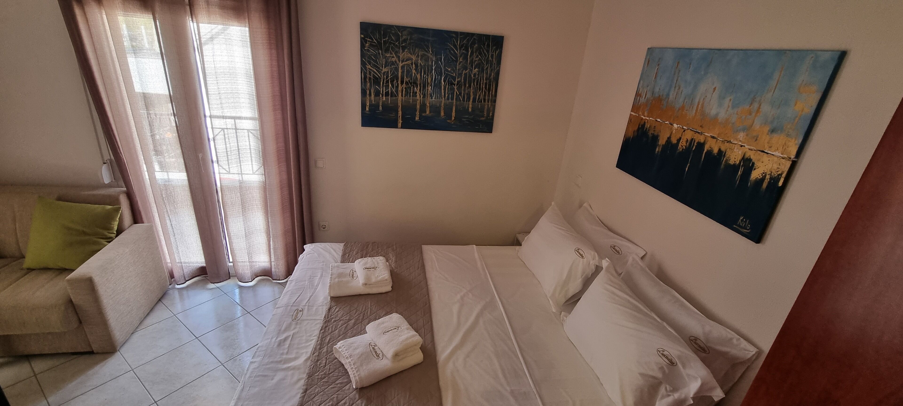 Un dormitorio ordenado con una cama, un sofá y dos cuadros en las paredes.