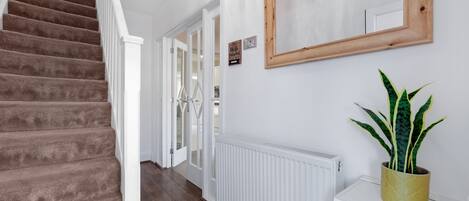 A staircase with carpeted steps, a white radiator, a potted plant, and a mirror on the wall.
