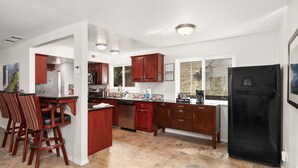A modern kitchen with dark wooden cabinets, a black refrigerator, and a bar area with stools. - New! Rivertop Hideaway with big views/spa/games/privacy! (Ahwahnee)