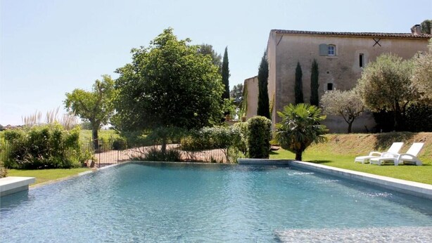 A rectangular swimming pool with clear blue water, surrounded by a well-maintained lawn and a variety of trees and shrubs. There are two white lounge chairs on the right side of the pool. - Gîte Tilleul - in the Provencal farmhouse of Domaine Faverot (Maubec)