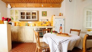 A kitchen with wooden cabinets, a tiled backsplash, a dining table with chairs, and a refrigerator. - Gîte Tilleul - in the Provencal farmhouse of Domaine Faverot (Maubec)