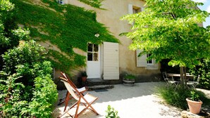 A courtyard with a wooden chair, a door, and a small table. - Gîte Tilleul - in the Provencal farmhouse of Domaine Faverot (Maubec)