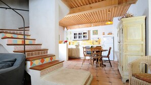 A kitchen with a dining area, wooden staircase, and a wicker chair. - Gîte Tilleul - in the Provencal farmhouse of Domaine Faverot (Maubec)
