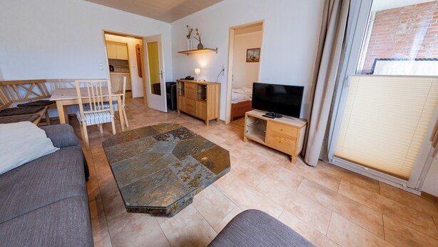 Una sala de estar con sofá, una mesa de centro, televisión, aparador de madera y un comedor con mesa y sillas.
