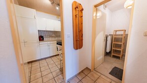 Una cocina con armarios blancos, piso de baldosas y puerta de madera.