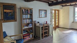 Een kamer met een houten boekenkast, een bureau met stoel, een lijst met afbeelding en een deur naar een andere kamer.