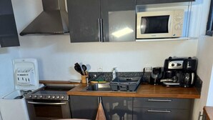 Una cucina compatta con forno a microonde, fornello e lavello. C'è un tavolo con tovaglia e una sedia con cuscino decorato.