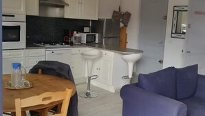 Un espacio habitable compacto con kitchenette, una zona de comedor con mesa y sillas, y un área de estar con sofá.