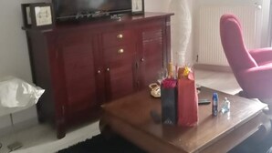 Un salón con un mueble bajo de madera oscura, un televisor encima, una silla roja y una mesita de centro con varios objetos.