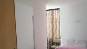 Un dormitorio con cama, una silla, armario y ventana con cortinas.