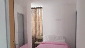 Un dormitorio con una cama, una silla, un espejo y una ventana con cortinas.