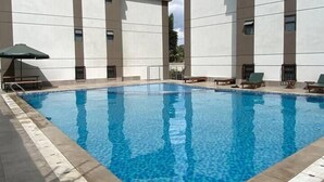 Une piscine dotée de chaises longues et d’un parasol, entourée d’un bâtiment au design moderne.