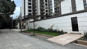 Un immeuble résidentiel à plusieurs étages, doté de balcons, d’une allée et d’un petit jardin.