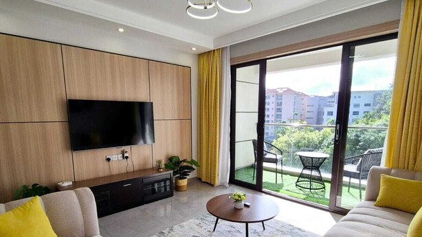 Un salon moderne doté d’un téléviseur à écran plat, de canapés avec des coussins jaunes, d’une table basse et d’un balcon aménagé avec du mobilier d’extérieur.