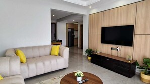 Un salon moderne avec un canapé beige, une table basse ronde et un grand téléviseur à écran plat fixé sur un mur recouvert de panneaux en bois.