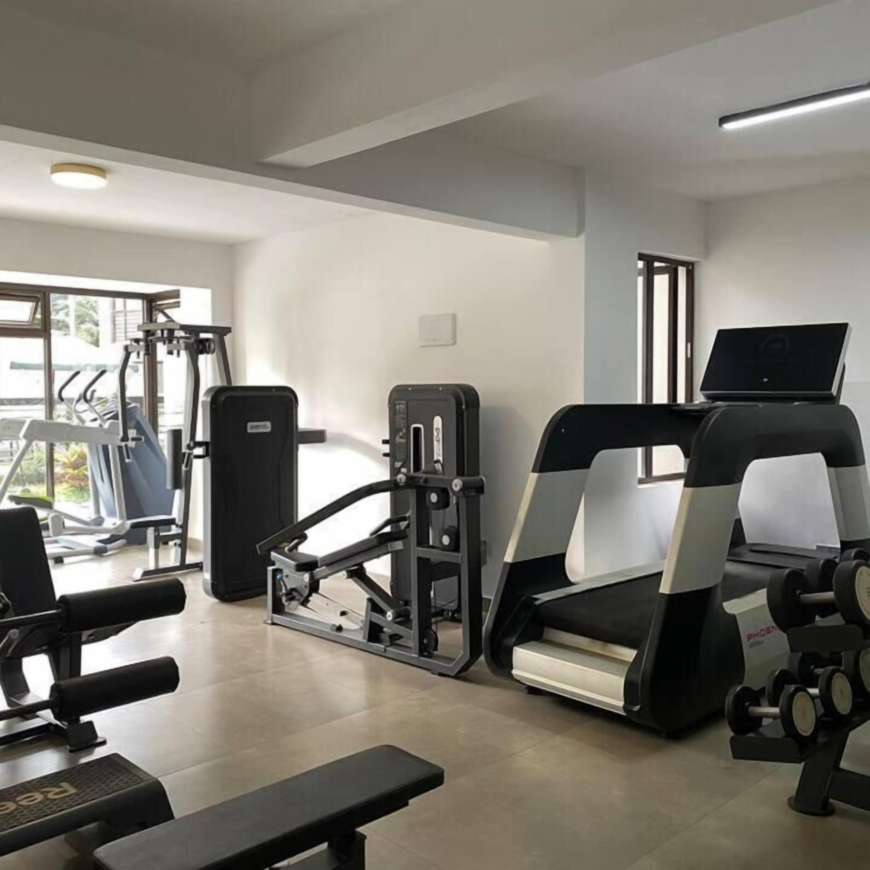 A gym with exercise equipment including treadmills, weight machines, and a bench.