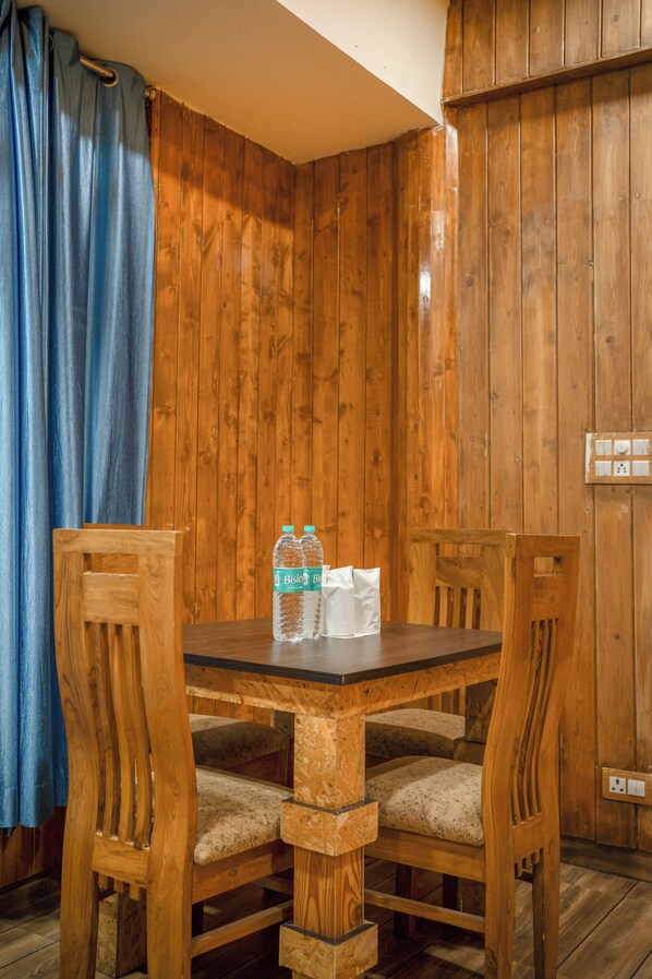 A wooden dining table with four chairs, a bottle of Biscal beer, and a tissue box. - Hotel Auli'D (Joshimath)