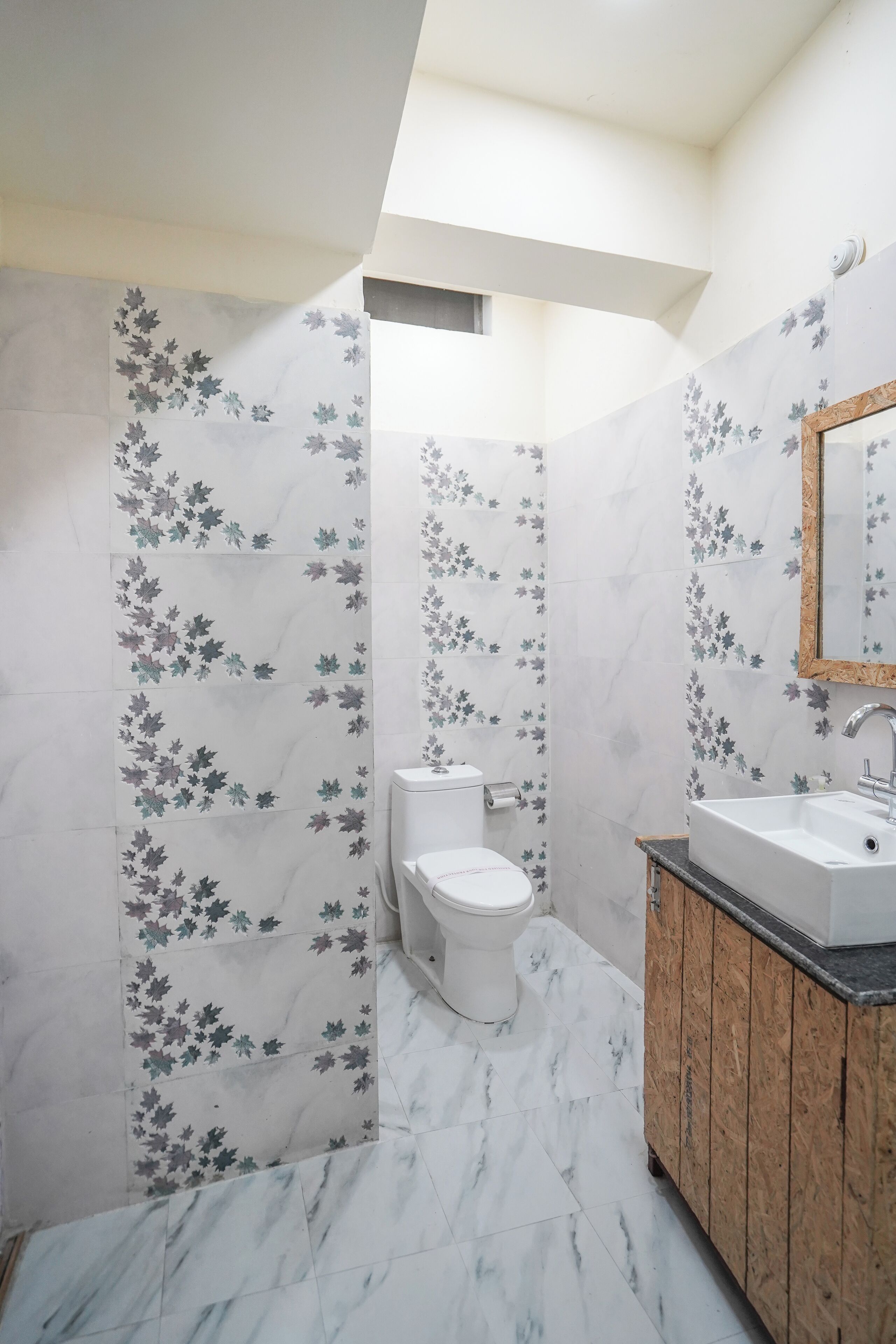 Een badkamer met toilet, wastafel en spiegel. De muren zijn betegeld met een bloemenpatroon.
