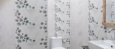Een badkamer met toilet, wastafel en spiegel. De muren zijn betegeld met een bloemenpatroon.