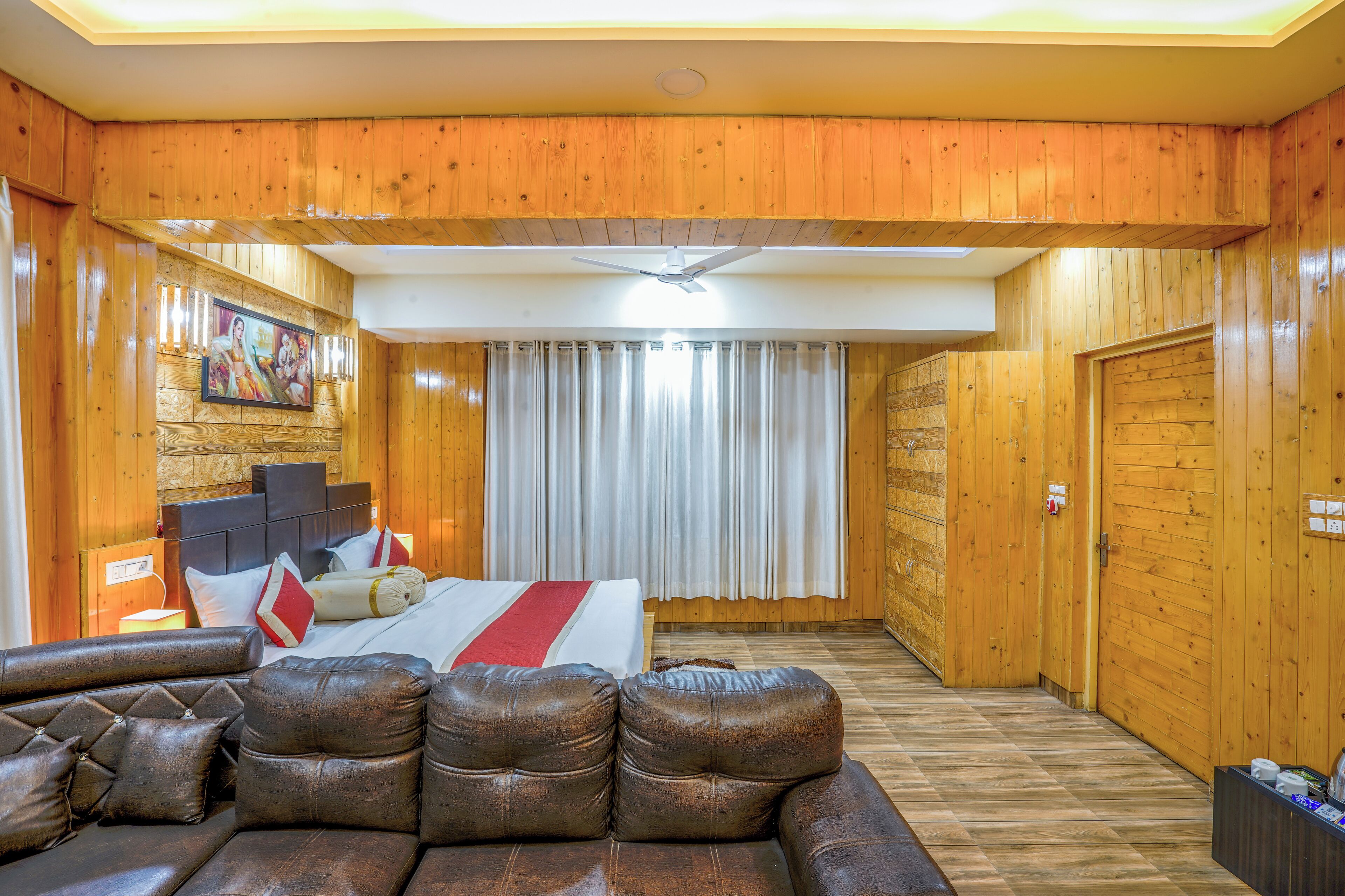 A wooden-paneled room with a bed, a leather sofa, and a ceiling fan.