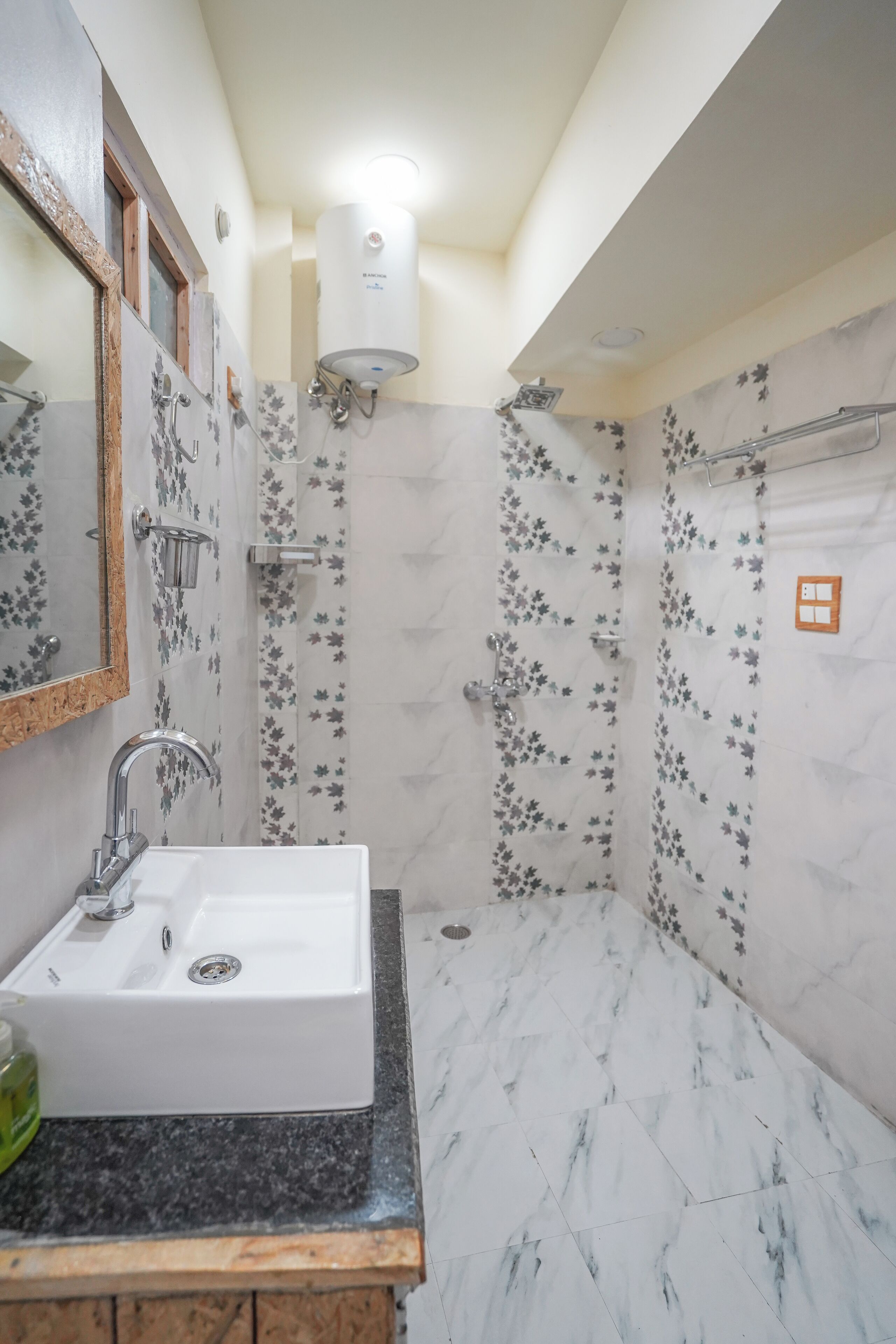 Ein Badezimmer mit einem weißen Waschbecken, einem Spiegel, einer Dusche mit floralen Fliesen und einem weißen Warmwasserbereiter.