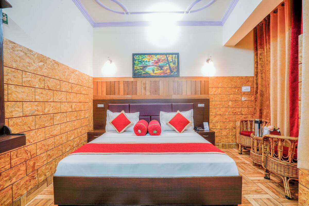 Une chambre d’hôtel avec une tête de lit en bois, un lit avec une literie rouge et blanche, un tableau au-dessus du lit et des meubles en osier.