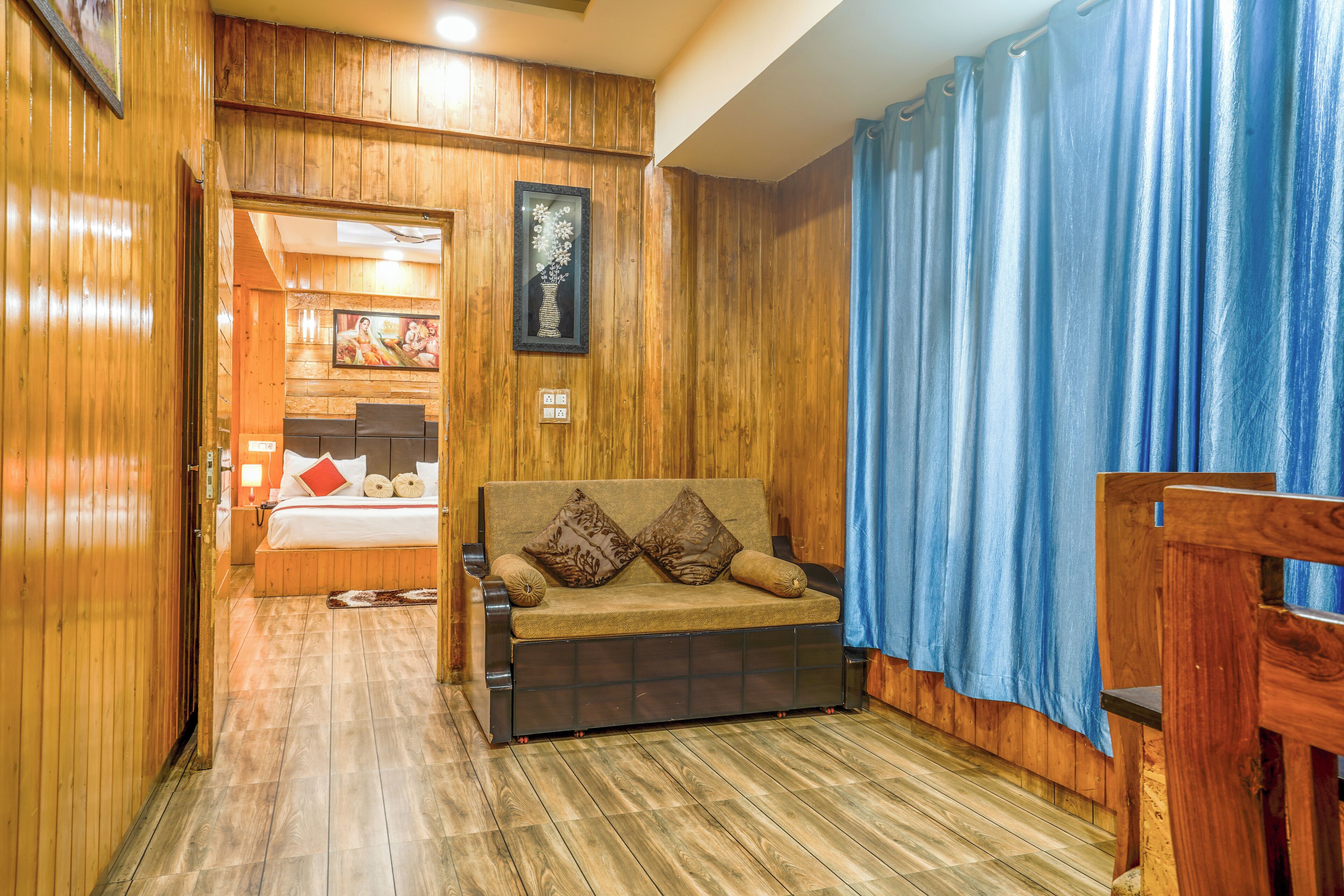 A wooden-floored room with a sofa, a bed, and a blue curtain.