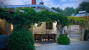 Un espace extérieur abrité, aménagé pour les repas, avec une table et des chaises, un mur en pierre et une cheminée en briques.