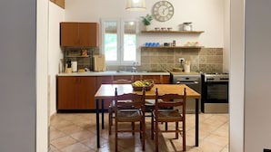 Une cuisine avec des meubles de rangement en bois, une table à manger avec des chaises, un luminaire suspendu, une horloge et une cuisinière.