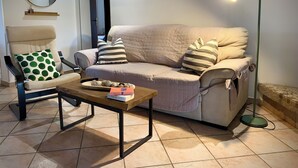 Un salon avec un canapé beige, un fauteuil orné d’un coussin à pois verts, une table basse en bois, un lampadaire et un miroir accroché au mur.