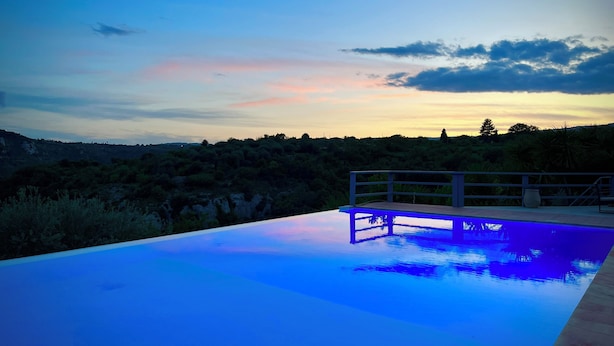 Une piscine offrant une vue sur un paysage vallonné au coucher du soleil.